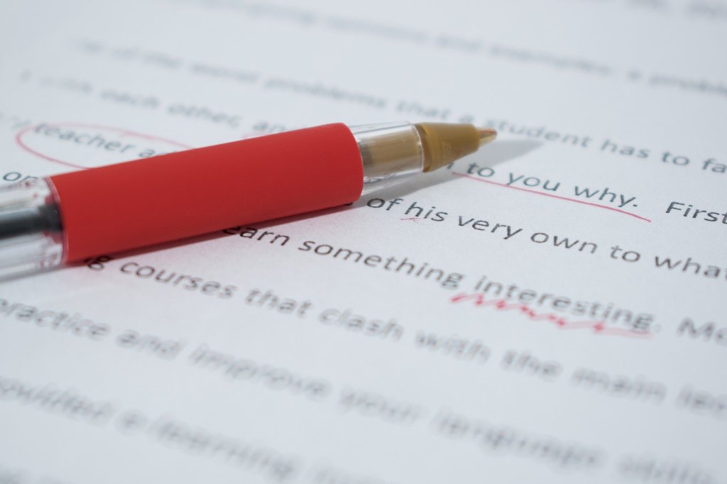 Red pen lying beside a page of writing with some markings and corrections.